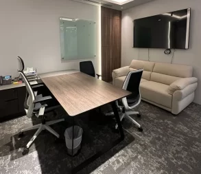 Spacious office with a large desk, meeting chairs, sofa, and wall-mounted TV for presentations.